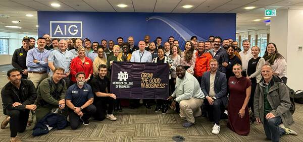 A large group of smiling professionals poses with a purple Mendoza College of Business banner reading