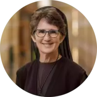 Smiling woman in glasses with short brown hair, wearing a black habit.