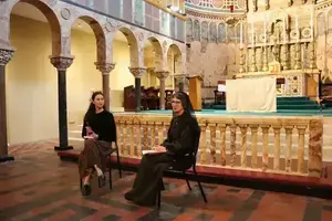 A nun in black speaks to a woman holding a microphone in Notre Dame's Newman University Church.