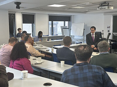 Man in suit presents to seated audience in classroom.
